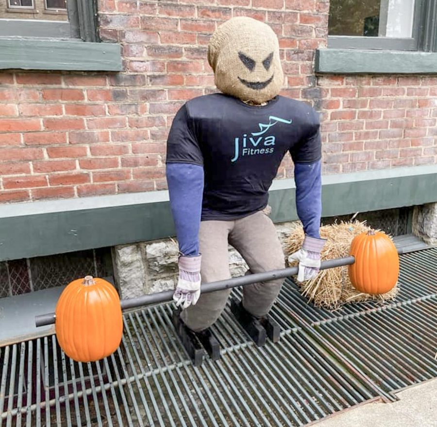 Scarecrow holding a barbell made of pumpkins.