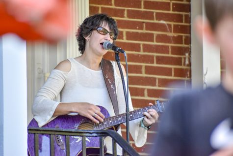 A woman playing a purple guitar and singing in front of a brick building.