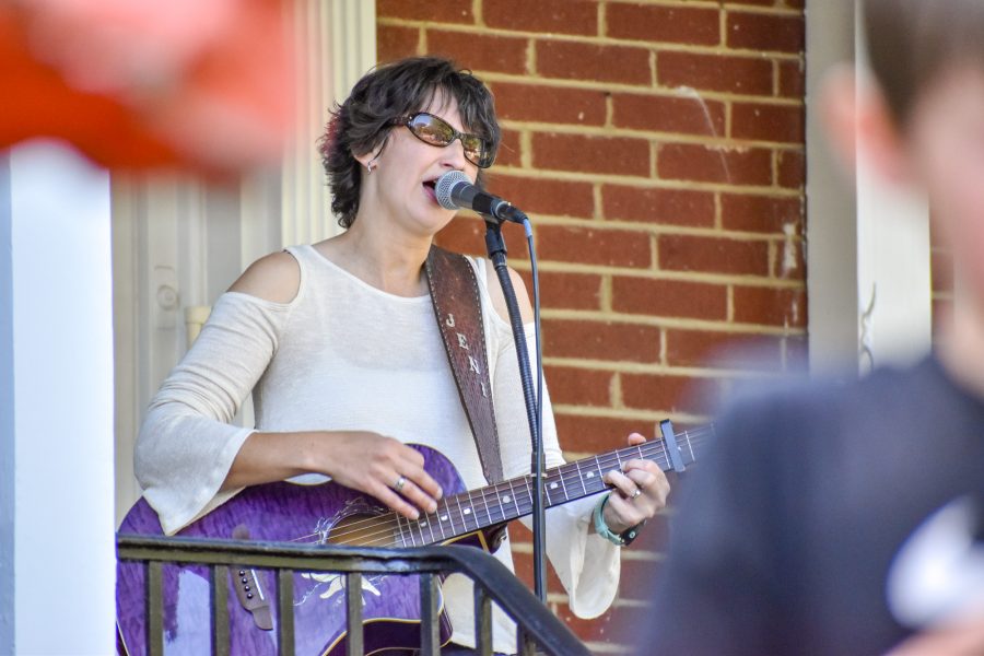 A+woman+playing+a+purple+guitar+and+singing+in+front+of+a+brick+building.