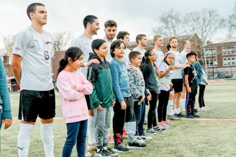 The mens soccer team stands alongside some of the elementary school students they have spent the semester doing community service with at the Earn Your Spots book club game. (Photo courtesy of Benji Grossi 23)